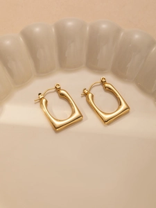 Detailed view of gold-plated U-shaped steel earrings on a textured ceramic display