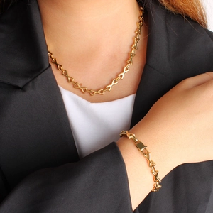 Parure collier et bracelet à maillons en X plaqué or 18K portée sur un costume noir