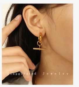 Gros plan de boucles d'oreilles dorées avec fermoir OT portées par un mannequin de style moderne