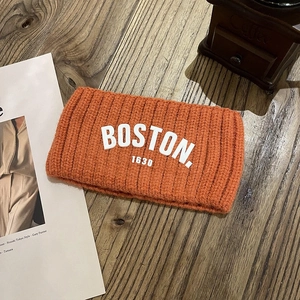 Détail du bandeau tricoté orange avec broderie Boston blanche sur fond en bois