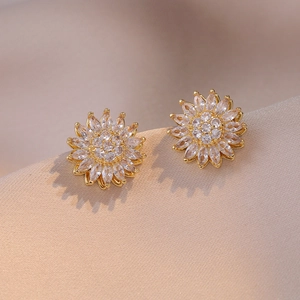 Macro shot of sparkling sunflower stud earrings with zircon petals on silk fabric