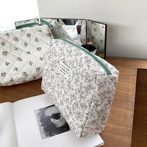 Detailed close-up of a quilted floral makeup bag with a green zipper on a wooden desk