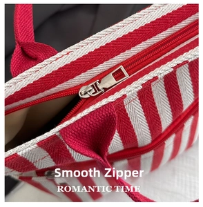 Close-up of durable metal zipper and red striped canvas texture on the tote bag