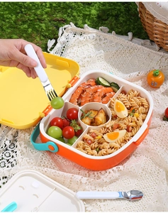 Outdoor picnic scene with a 5-compartment portable lunch box featuring an orange and yellow design