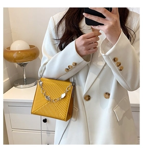 Detail of ginger yellow PU handbag featuring textured diagonal patterns and silver chain