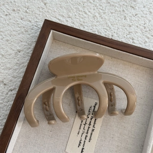 Detail of milk tea hair claw clip with golden text engraving in a wooden display tray