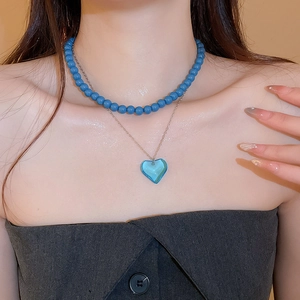 Close-up of double layer necklace featuring blue bead choker and heart pendant chain