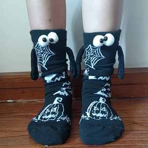 Detail of black Halloween socks with 3D eyes, tiny hands, and knit pumpkin patterns