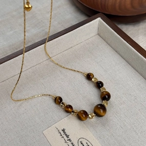 Macro shot of tiger eye beads and gold heart pendant on a chain in a jewelry display box