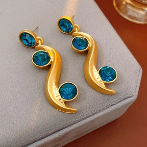 Detailed shot of vintage gold wave earrings with blue crystals on velvet jewelry box