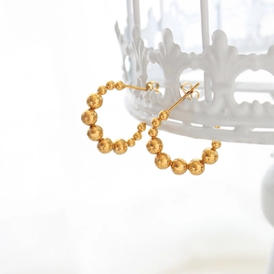 Boucles d'oreilles créoles perlées en or en forme de C sur un support blanc
