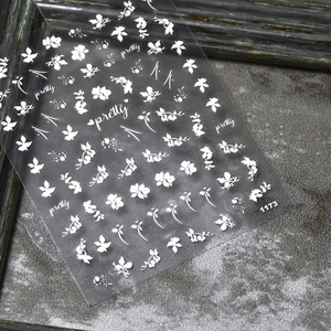 Detail of white 5D nail art stickers featuring flowers and butterflies on dark stone surface