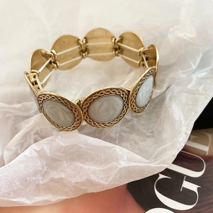 Close-up of golden round charms with mother of pearl inlay on an elastic bracelet