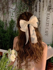 Detail of cream tulle bow hair clip with long ribbons on a model in a cafe