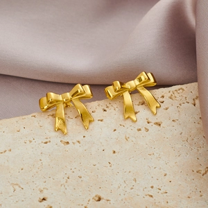 Detailed view of elegant gold bow earrings on ivory stone and pink velvet background