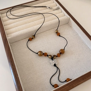 Detail of faux leather necklace with brown beads and silver butterfly pendant in wooden tray
