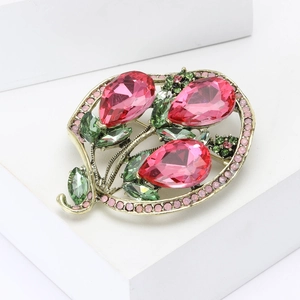 Vintage gold brooch with three pink teardrop gems and green rhinestones on white background