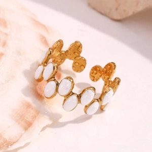 Detail of 18K gold-plated open ring with white enamel ovals on a shell with water drops