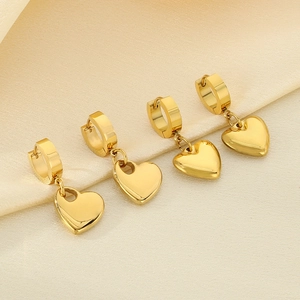 Detailed view of gold-tone hollow heart earrings on elegant champagne silk background