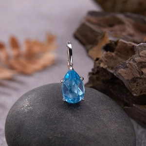 Macro detail of teardrop blue gemstone pendant set in silver on dark natural stone
