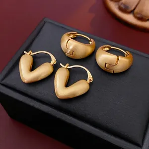 Brushed gold heart and V-shaped hoop earrings set displayed on a premium leather box