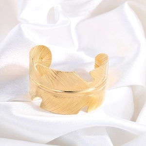 Macro shot of gold leaf feather bangle with delicate textures on white silk background