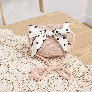 Detail of pink straw crossbody bag featuring a large polka dot bow on a lace mat