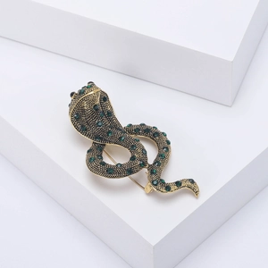 Macro detail of vintage gold cobra brooch with emerald green rhinestones and sturdy pin back