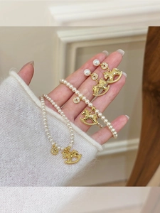 Detail of beaded pearl necklace with gold rocking horse pendant held by a model