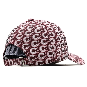 Detail view of burgundy baseball cap with white C pattern and silver metal buckle