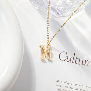Detailed shot of golden M initial necklace with zircon flower pendant on aesthetic background
