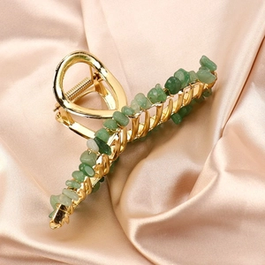 Close-up of gold alloy hair claw with green natural crystal stones on satin cloth