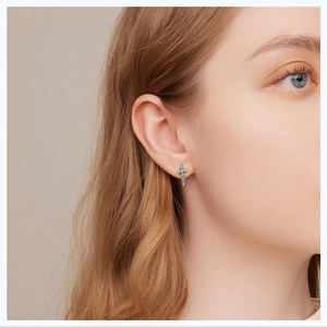 Close-up of sky blue cross earrings with zircon inlay worn on ear for elegant style