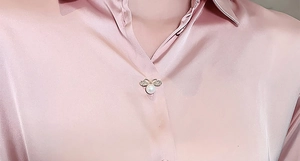 Vue macro d'une broche noeud dorée avec perles et zircons sur du satin rose