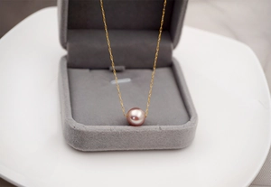 Pink pearl pendant on gold chain necklace resting in a grey velvet jewelry box