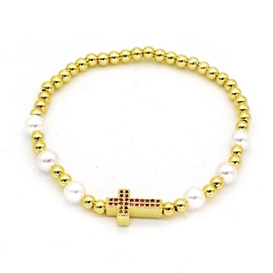 Golden bead and white pearl bracelet featuring a red zircon cross charm on a white background