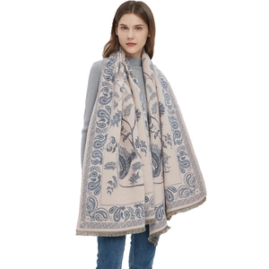Beige and blue paisley scarf with bird patterns and tassels on a female model