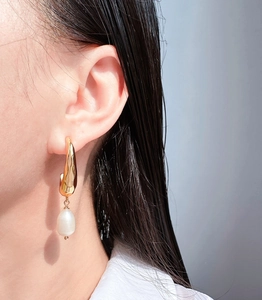 Close-up of elegant hammered gold geometric earrings with a baroque pearl drop on model