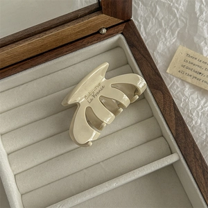 Macro detail of cream oval hair claw clip with golden lettering in a premium gift box