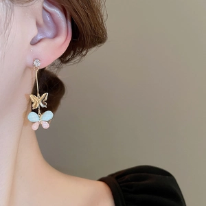 Close-up of dangling butterfly earrings featuring gold finish with pink and blue resin wings