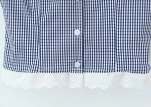 Close-up of blue gingham shirt with white round buttons and delicate lace embroidery hem