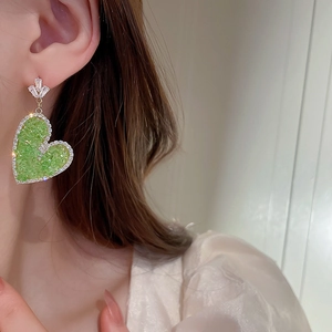 Detailed close-up of green heart earrings with sparkling crystals on a model's ear