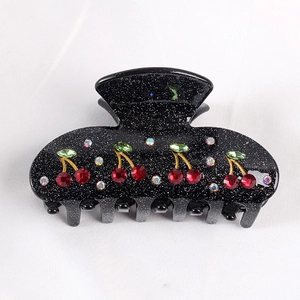 Glittery black claw clip with red rhinestone cherry pattern on white fabric background