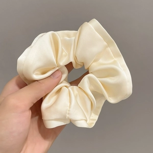 Detailed view of cream satin scrunchie showing glossy fabric texture and ruffled edges