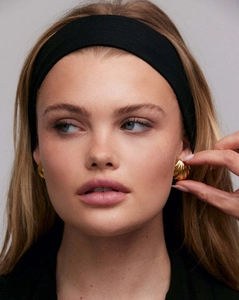 Close-up of golden shell-shaped earrings and a wide black elastic headband on a model