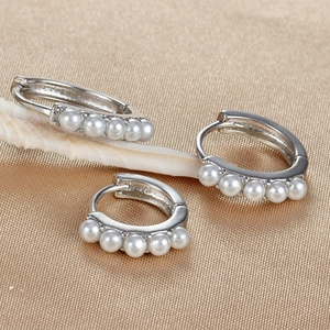 Close-up of three 18K plated silver hoop earrings with white pearls on golden fabric