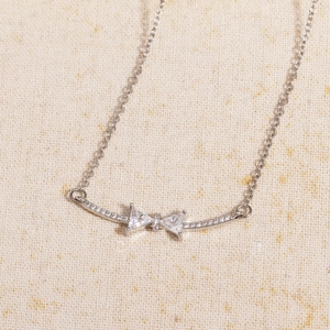 Macro shot of silver bow necklace pendant with sparkling cubic zirconia on fabric background