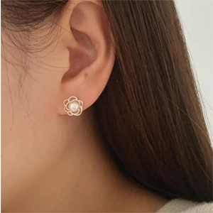 Detail of flower-shaped pearl stud earring with gold petals worn on model ear
