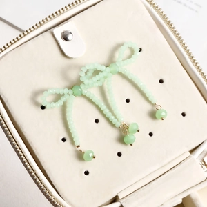 Detail of light green beaded bow jewelry with gold hardware inside a white leather jewelry box