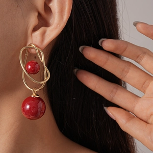 Close-up of geometric gold wire wrapped red resin ball drop earrings worn by a model